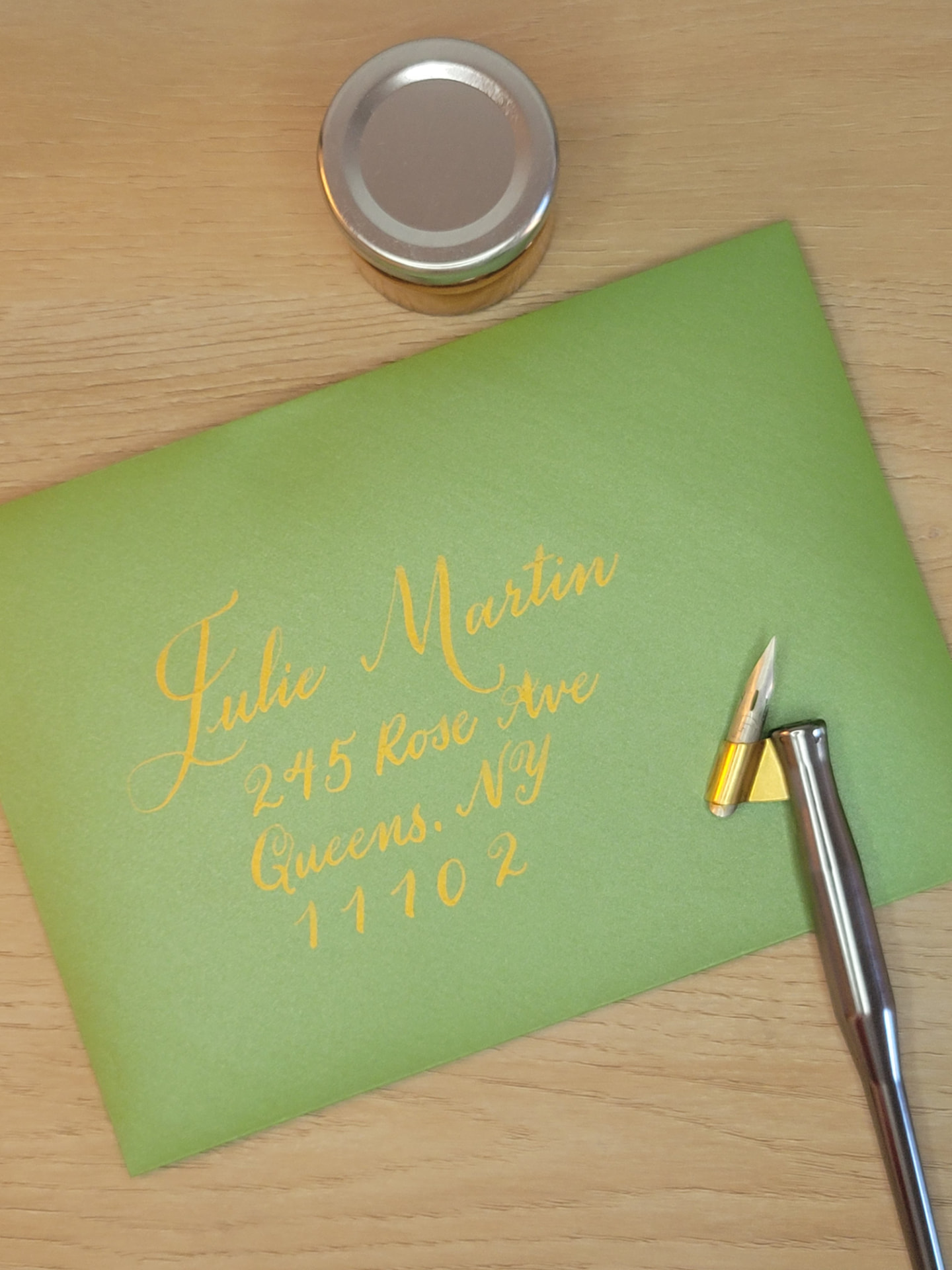 Gold calligraphy addressed on a green envelope beside a dip pen